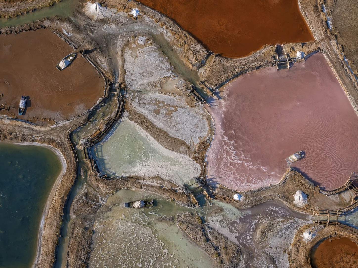 Salt ponds from above in rust, rose, petrol and mineral white with narrow paths