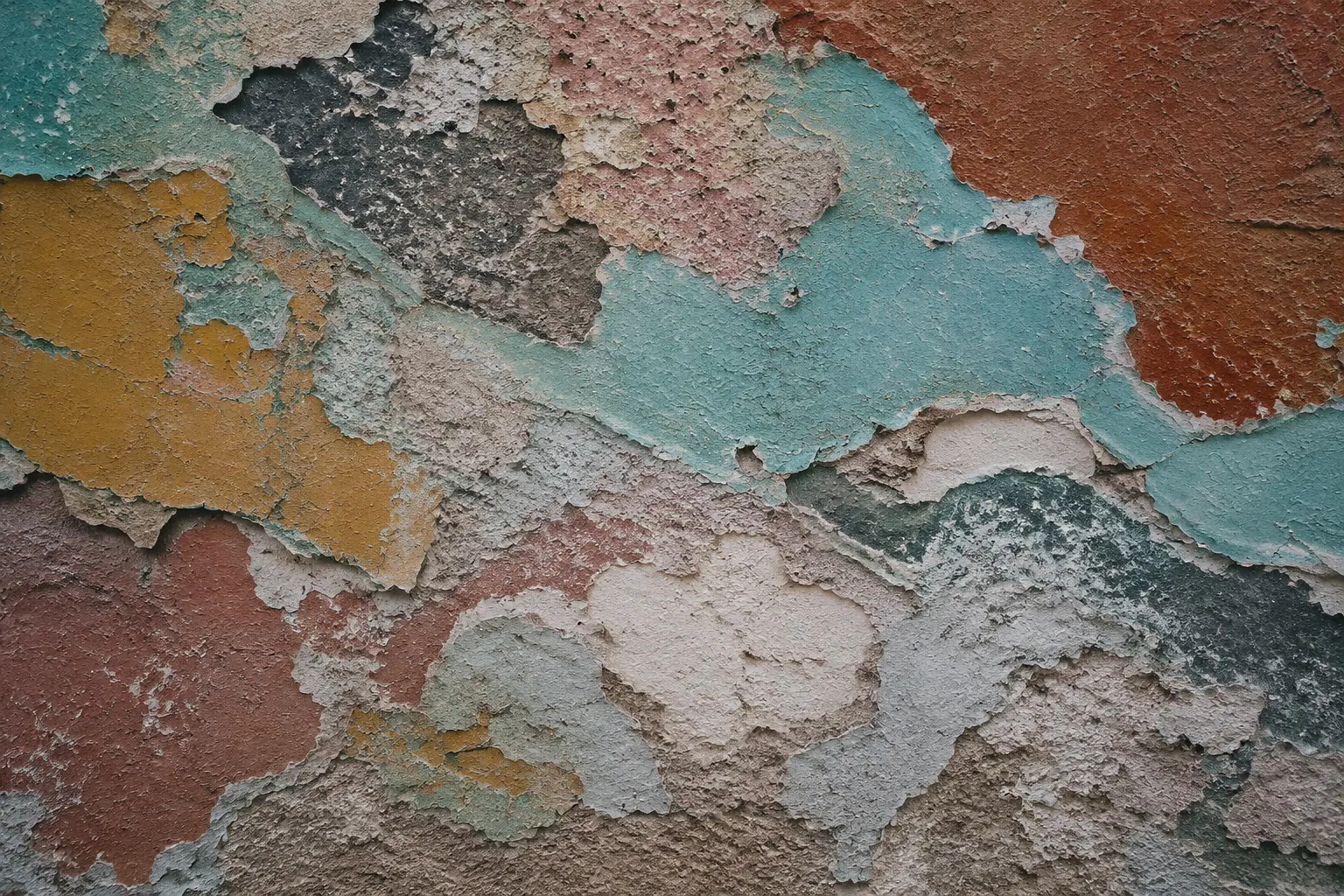Old wall with peeling layers of turquoise, terracotta, ochre, rose and chalk-white paint